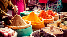 Bunte Gewürzhaufen wie Kurkuma, Paprika und Kräuter in offenen Säcken auf lebhaftem Markt.