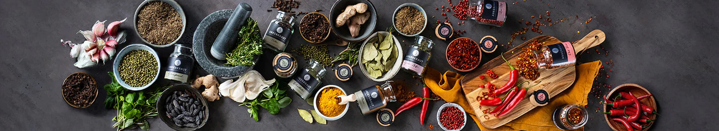 Offene, liegende Ankerkraut Korkengläser inmitten von Mösern und Schälchen mit Rohgewürzen wie Pfefferkörnern und Chilischoten.