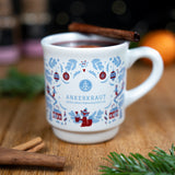 Tasse mit heißem Getränk und Zimtstange, bedruckt mit winterlichen Motiven auf Holztisch.