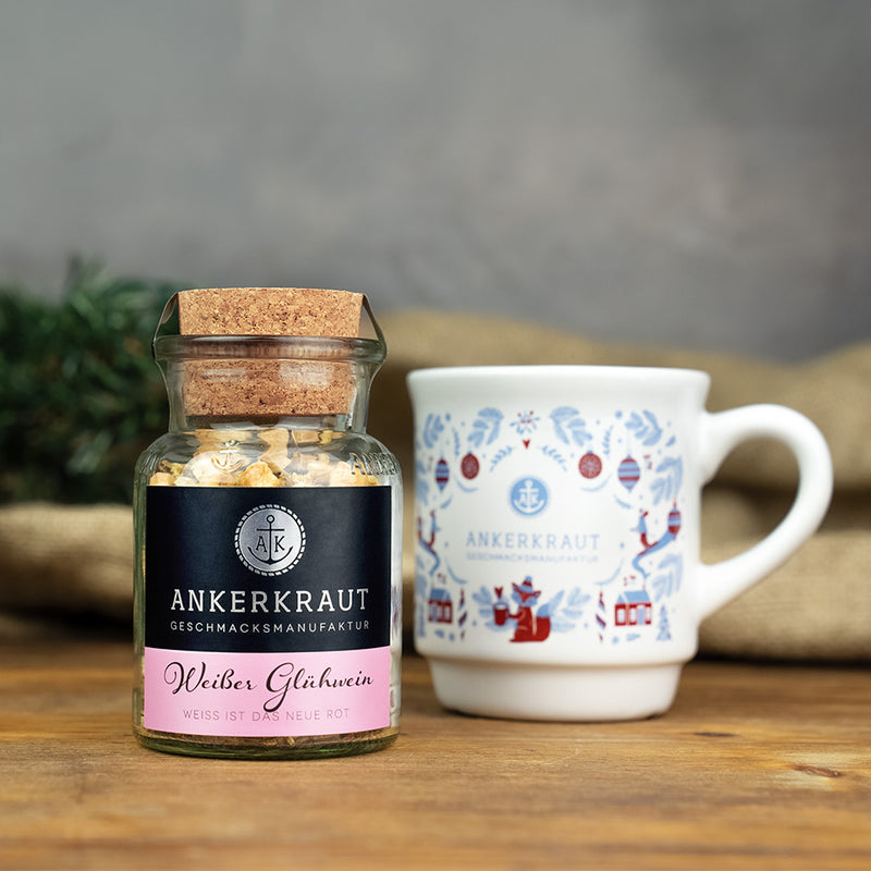 Weißes Glühweingewürz von Ankerkraut neben Tasse mit weihnachtlichen Motiven auf Holzuntergrund.