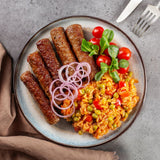 Cevapcici mit Djuvec-Reis, roten Zwiebeln und Tomaten, angerichtet auf Teller mit frischem Feldsalat.
