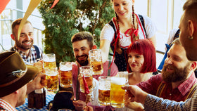 Eine Gruppe Freunde im Oktoberfest-Outfit stößt mit Bierkrügen an.