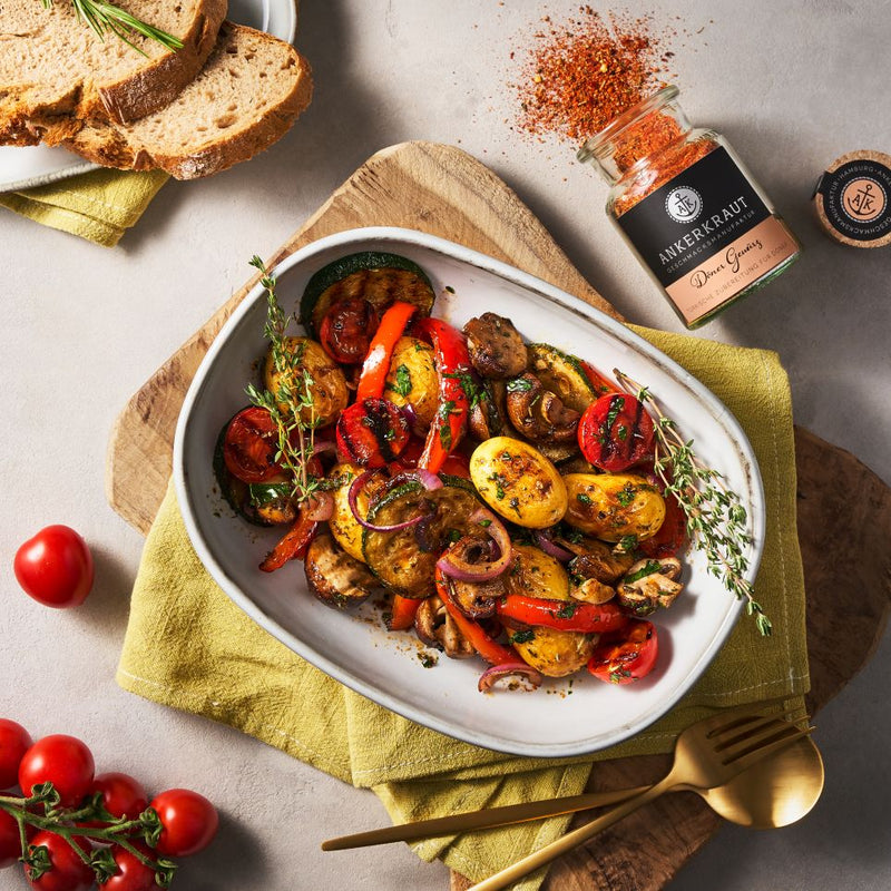 Ofengemüse mit Kartoffeln, Paprika, Zucchini und Champignons in Auflaufform, daneben Döner Gewürz und Brot.