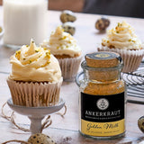 Cupcakes mit hellem Frosting und Pistazien, daneben Golden-Milk-Gewürzglas auf dekoriertem Tisch.