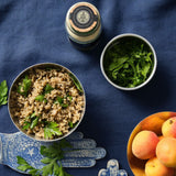Linsen-Bulgur-GEmüse mit Petersilie in Schale, dazu frische Kräuter, Aprikosen und Gewürzglas auf blauem Stoffhintergrund.