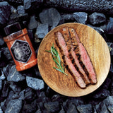 Magic Dust Rub neben einem frisch gegrillten und filetierten Steak auf einem Holzteller.