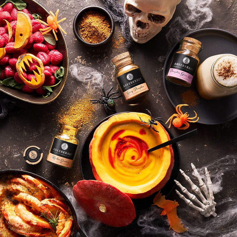 Halloween-Dekoration mit Kürbissuppe, Pumpkin-Spice-Latte-Gewürzen und pinken Gnocchi, inszeniert mit Totenkopf und Spinnen.