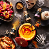 Halloween-Dekoration mit Kürbissuppe, Pumpkin-Spice-Latte-Gewürzen und pinken Gnocchi, inszeniert mit Totenkopf und Spinnen.
