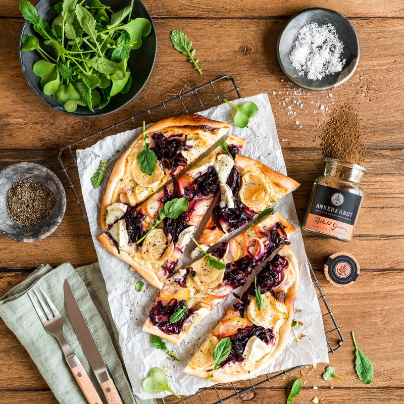 Flammkuchen mit Rotkohl, Ziegenkäse und Kräutern, daneben Rotkohl Gewürz auf rustikalem Holztisch.