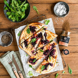 Flammkuchen mit Rotkohl, Ziegenkäse und Kräutern, daneben Rotkohl Gewürz auf rustikalem Holztisch.