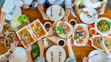 Mehrere Personen sitzen am Tisch und teilen verschiedene asiatische Gerichte wie Nudeln, Fleisch und Gemüse.
