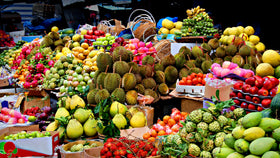 Marktstand mit tropischen Früchten wie Durian, Mango, Bananen und Rambutan in großen Körben und Kisten.