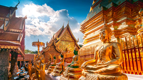 Goldene Buddha-Statuen vor kunstvoll verziertem Tempelgebäude unter blauem Himmel und Sonnenlicht.