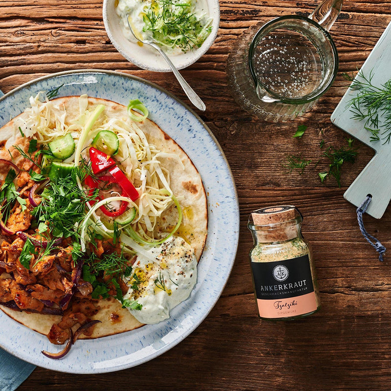 Gyros-Teller mit Fleisch, Tzatziki, Gemüse und Fladenbrot, daneben Tzatziki-Gewürz auf rustikalem Holztisch.